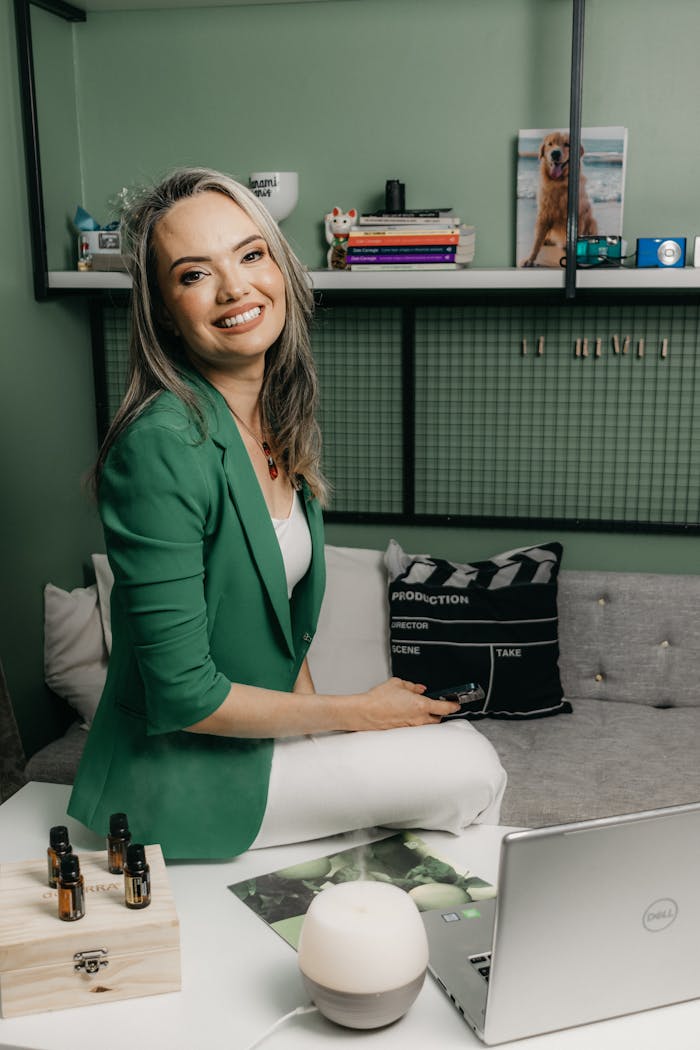 Elegant woman in a green jacket smiles while sitting at her office desk.